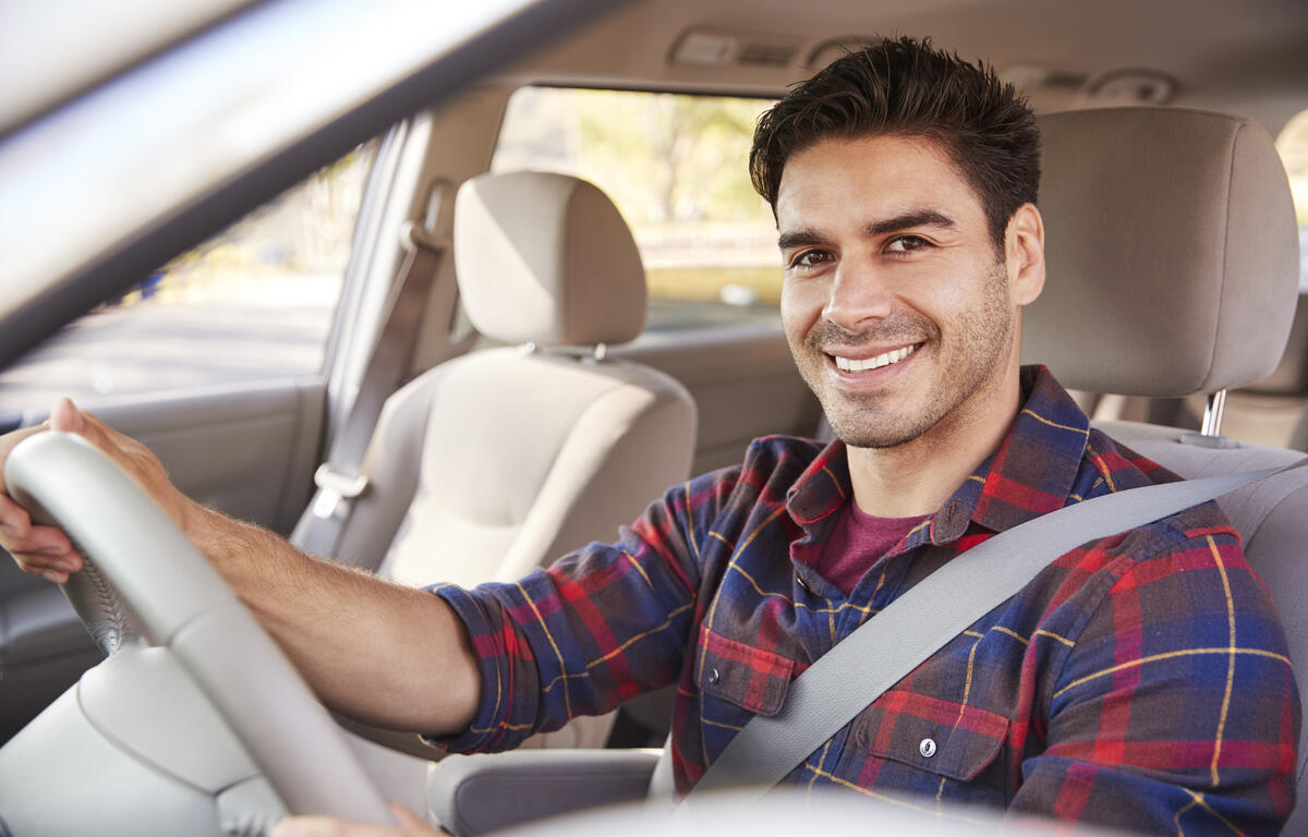 Young man in car driving seat looking to camera, portrait