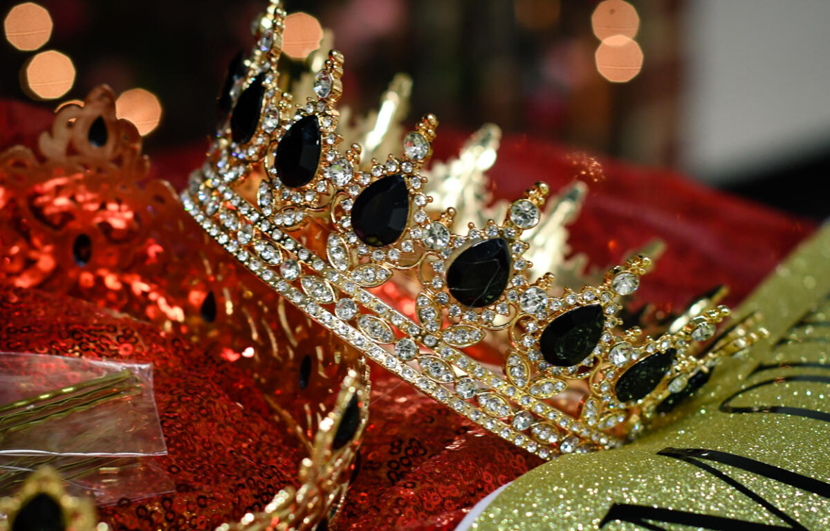Gold tiara encrusted with clear and black gemstones rests on red sequined fabric, glittery party decor in background