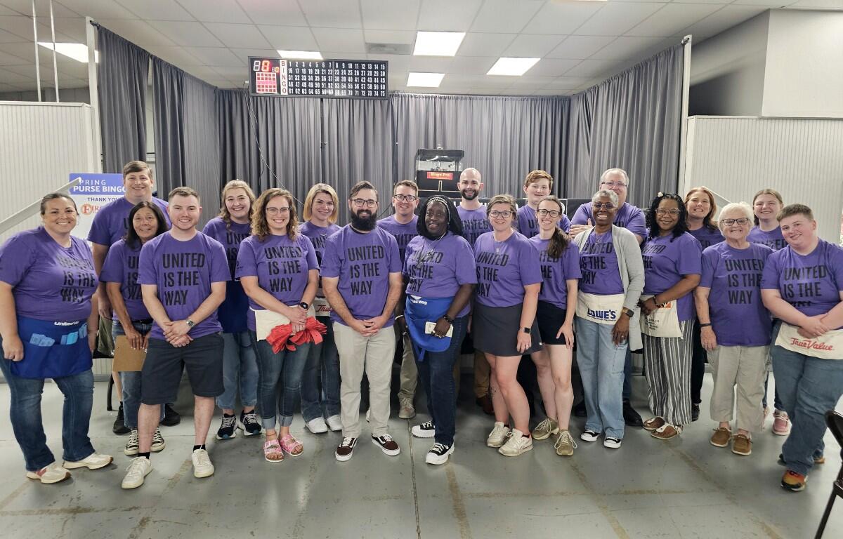 Group of people wearing purple shirts that read 'UNITED IS THE WAY' posing together in a bowling alley.