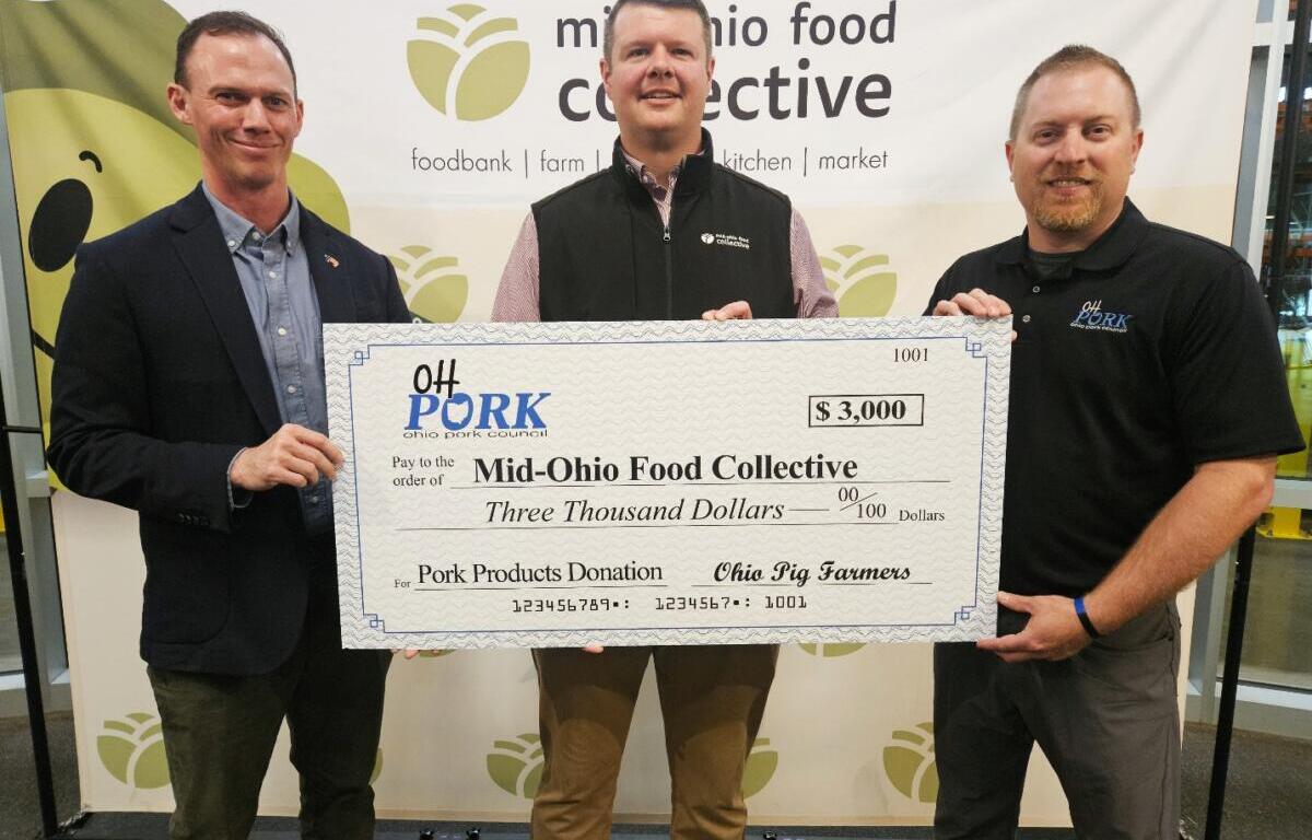 Three men hold a large ceremonial check for $3,000 to Mid-Ohio Food Collective, standing in front of a banner.
