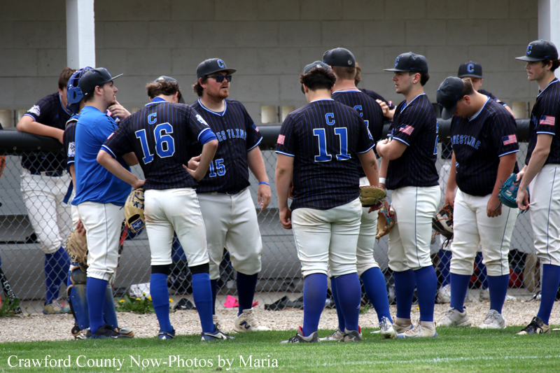 Baseball players in blue and white uniforms stand together in a huddle near the dugout on the field before a game.