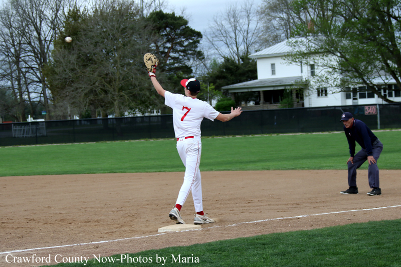 Baseball player in white uniform with number 7 throws from near first base during a game, ball in the air.