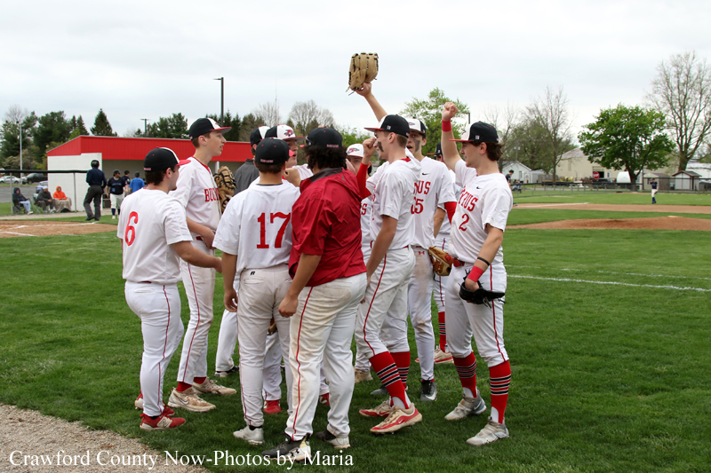 Baseball players in white and red uniforms huddle on the field, one player raises a glove in celebration.