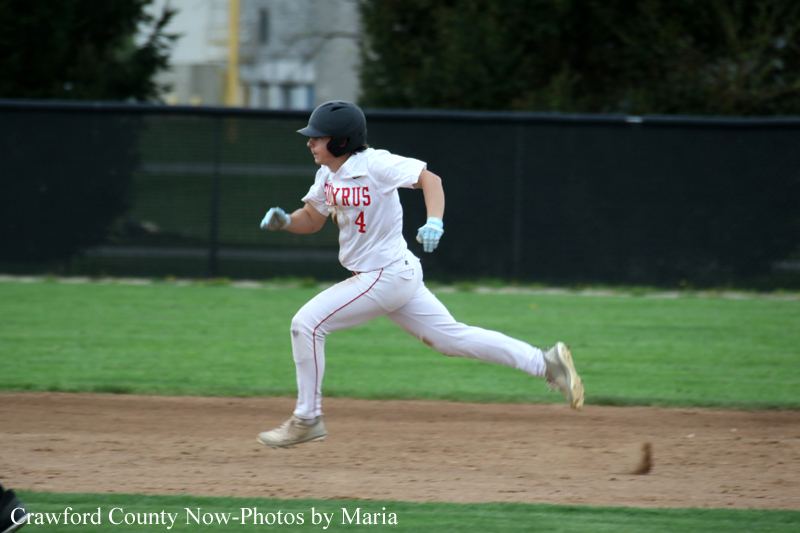 Baseball player sprinting on infield dirt in a white uniform with red lettering and a helmet, mid-run clutching a glove on his left hand to advance base.