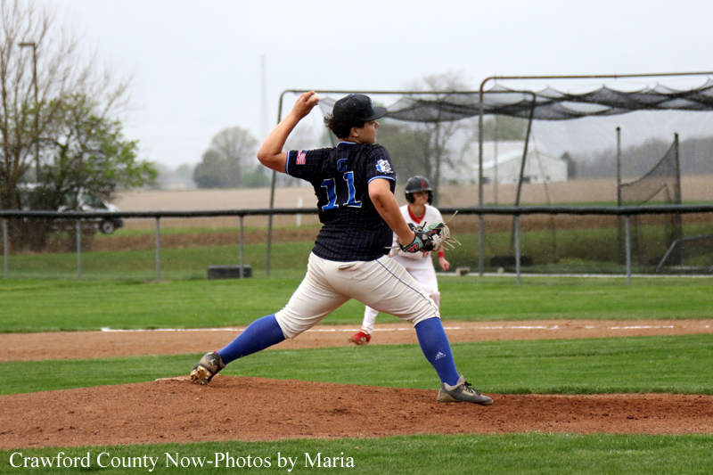 Baseball pitcher in a dark blue jersey (number 11) throwing from the mound as a catcher stands behind him on the field.