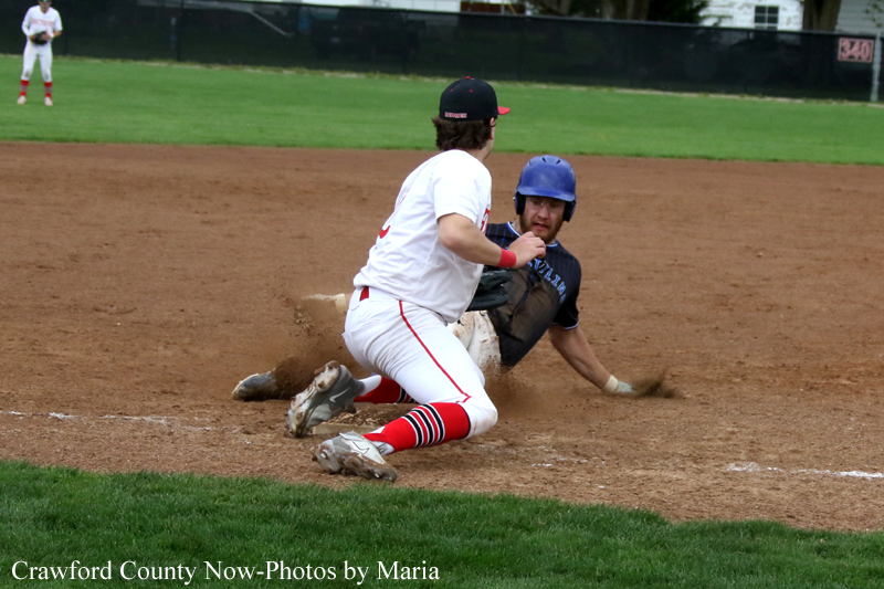 Baseball scene: a runner in white with red socks slides into a base as a fielder in a blue helmet reaches to tag him on the dirt.