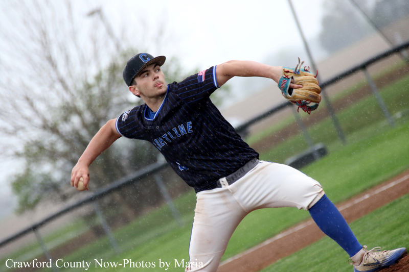 Male baseball pitcher in a dark blue jersey winds up to throw on a dirt mound, glove extended left.