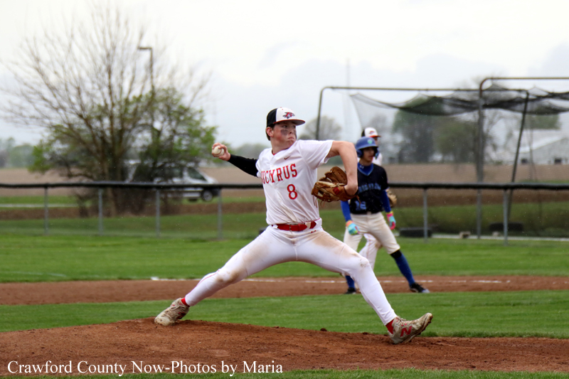 Baseball pitcher in a white uniform winding up on the mound as a catcher and fielders stand in the background.