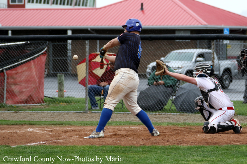 Baseball batter in a blue helmet swings at a pitch as the catcher crouches behind him in full gear.