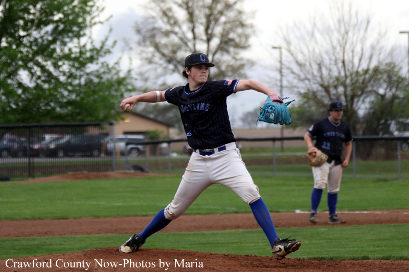 Baseball pitcher in a navy jersey throwing a pitch on the mound, with a fielder in the background.