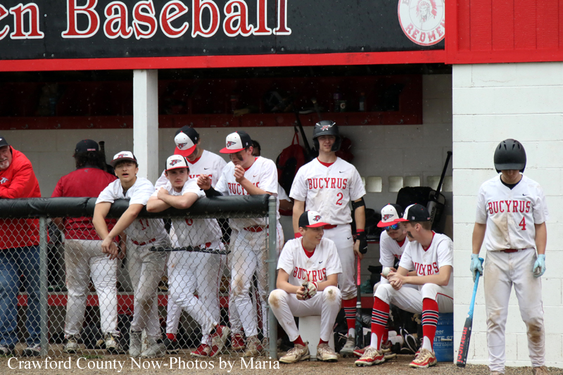 Youth baseball team in white Bucyrus uniforms leaning on a fence in the dugout, preparing for the game.