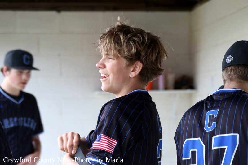 Smiling baseball player in a dark pinstriped uniform in the dugout, American flag patch on the sleeve.