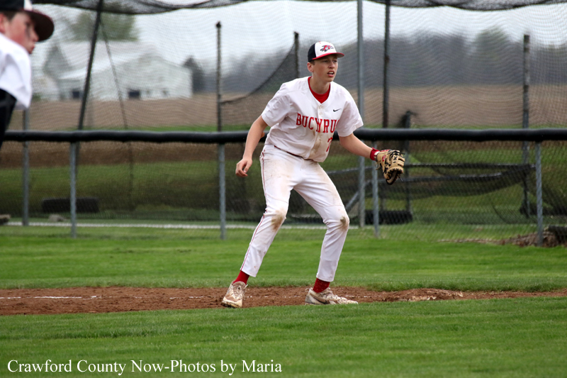 Baseball player in white and red uniform standing on the pitcher's mound with glove ready, Bucyrus on the chest, fence in background
