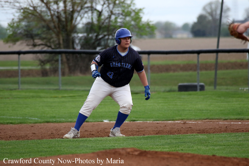 Baseball player in a blue uniform crouches on a dirt base, helmet on, gloves ready during a game.
