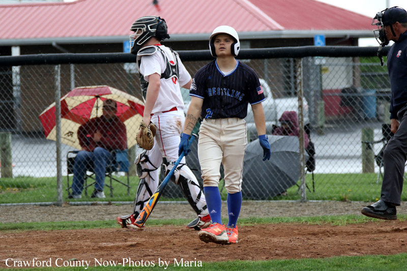 Young baseball player in a navy jersey and helmet stands at home plate as catcher and umpire watch from behind the fence.