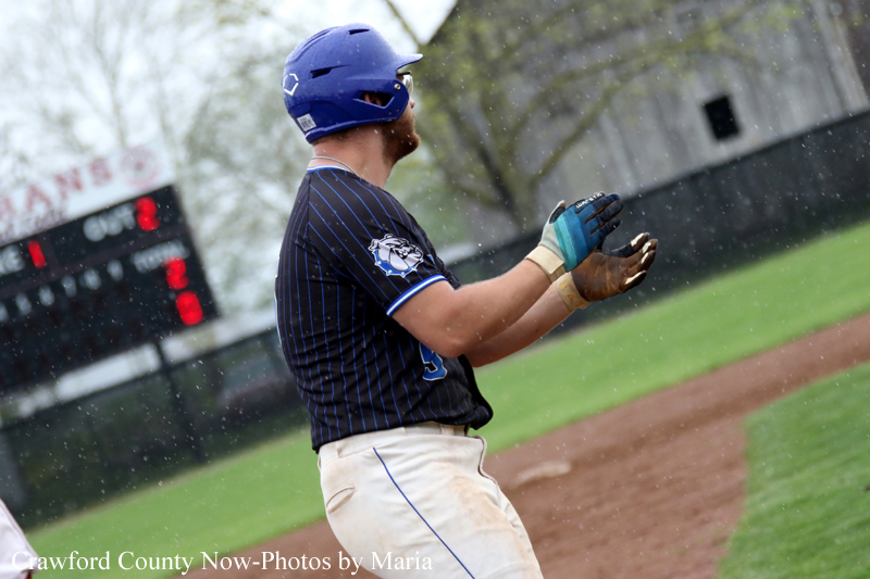 Baseball player in a blue helmet and pinstriped jersey claps hands on the infield during a game, with a scoreboard in the background.