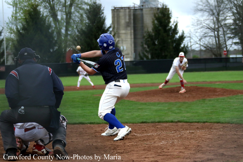 Baseball game action: batter in blue helmet and jersey swings at a pitch while the catcher crouches behind home plate; pitcher on the mound in the background.