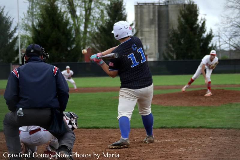 Baseball scene: batter wearing #11 swings at an in‑flight pitch as the catcher and umpire stand behind him on the infield dirt.