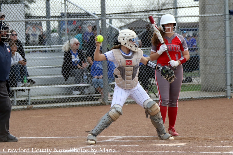 Girls' softball game: catcher in beige gear prepares to throw a pitch while batter in red stands at home plate.