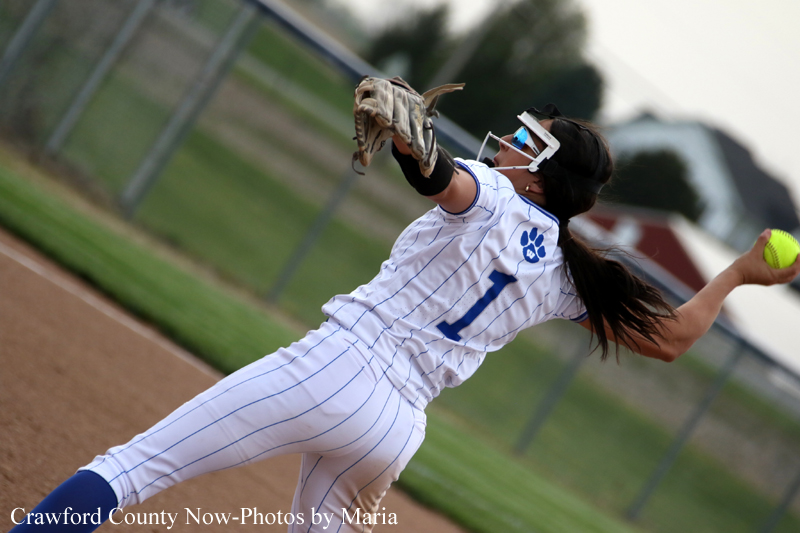 Woman softball pitcher in a white pinstripe uniform throwing a pitch on the infield.