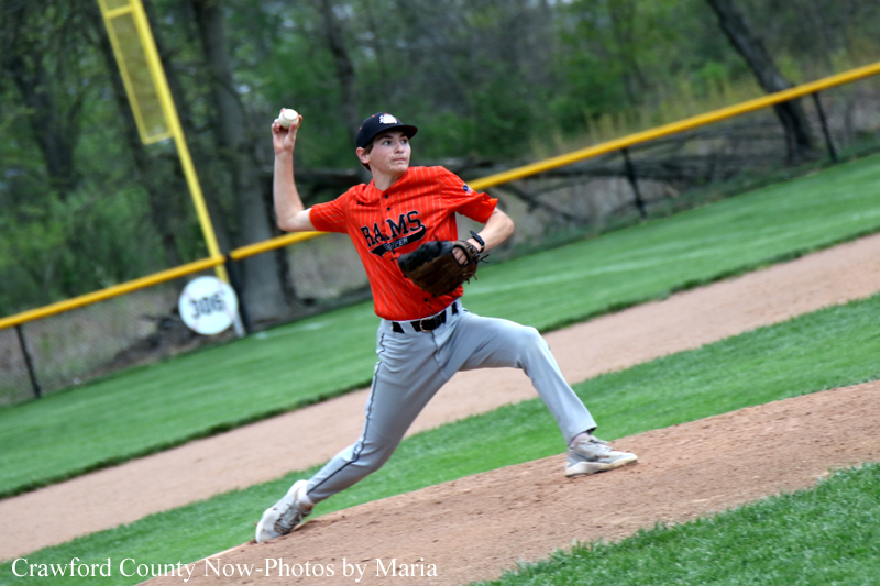 Baseball pitcher in orange uniform winding up to throw a pitch on the mound, mid-curl with glove ready.
