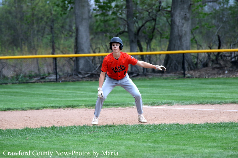 Youth baseball infielder in a red jersey and helmet, crouched and ready with glove on the dirt infield.