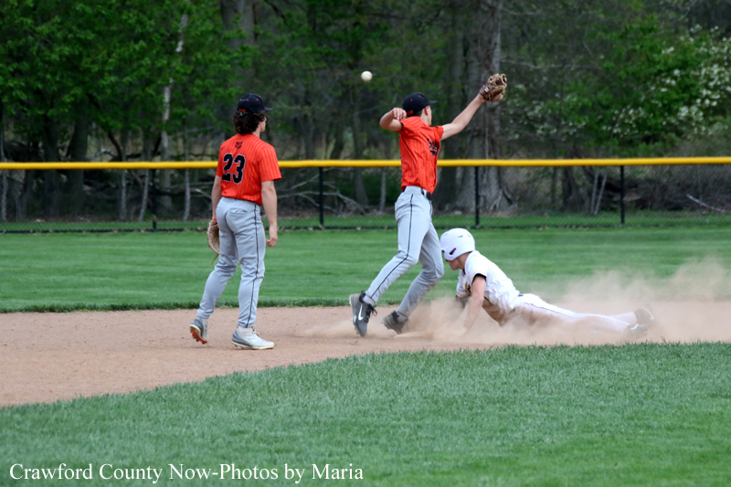 Baseball game: a runner slides into a base while a fielder reaches to tag, dust rising from the dirt as teammates watch nearby.