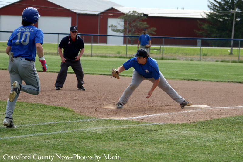 Baseball infield action with a blue-team fielder reaching to tag a runner at second base while an umpire watches in the background.