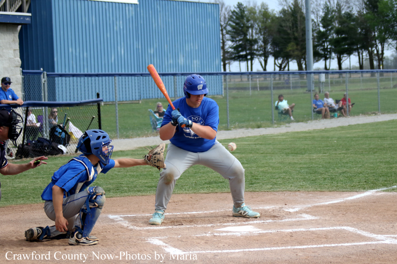 Youth baseball batter in blue swings at a pitch with a catcher in blue gear squatting behind home plate.
