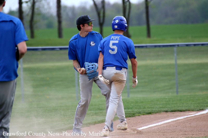 Two baseball players in blue jerseys stand on the dirt infield near the bases, one facing the other wearing a helmet with jersey number 5 (Pope).