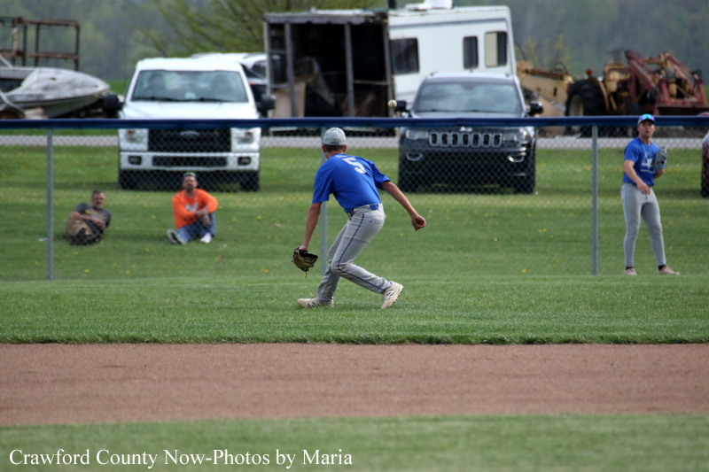 Baseball fielder in a blue jersey and gray pants fields a ground ball on the infield dirt near the grass.