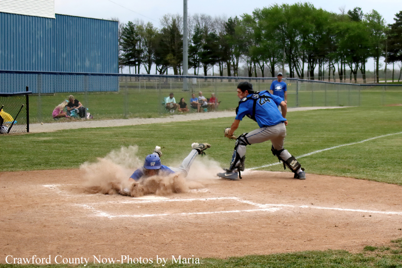 Baseball catcher in blue gear tags a sliding runner as dust flies at home plate in a youth game.
