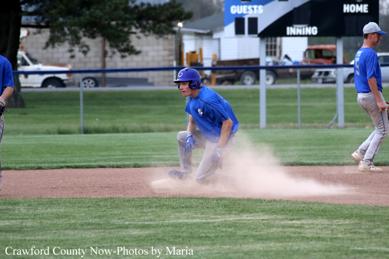Baseball player in a blue uniform slides into a base as dust rises from the infield dirt.