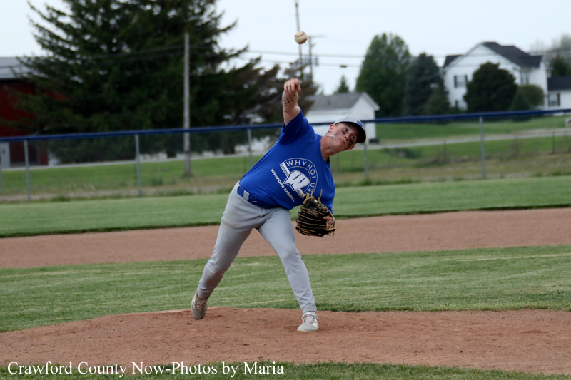 Baseball pitcher in a blue uniform winds up to throw on the mound, ball in the air.