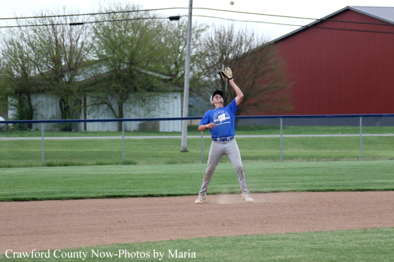 Baseball player in a blue jersey catches a ball with his glove above his head on a dirt infield.