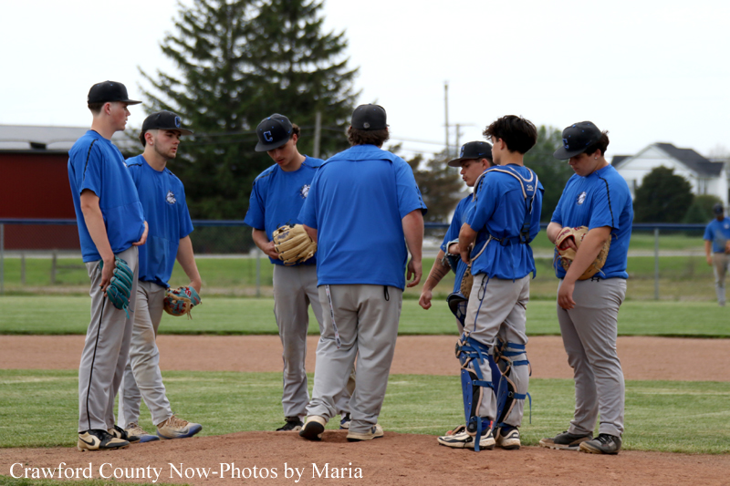 A group of baseball players in blue shirts gathering on the infield, talking and preparing for practice.