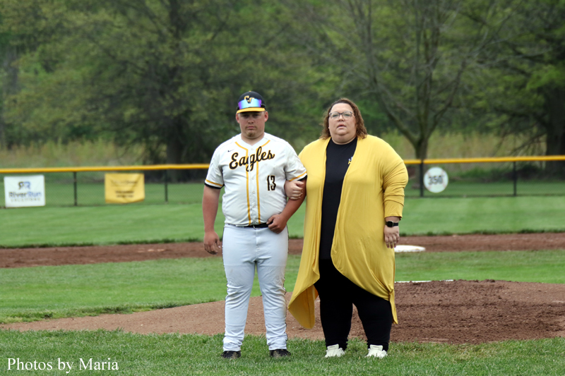 Baseball player in a white and yellow Eagles uniform stands with a woman in a yellow cardigan on a baseball field, arm in arm.