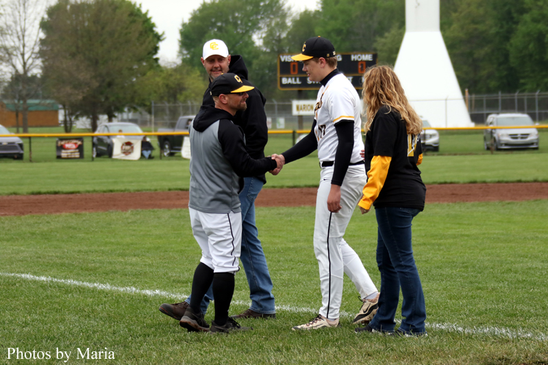 Two baseball players shake hands on the infield while a man and a woman watch in casual clothing.