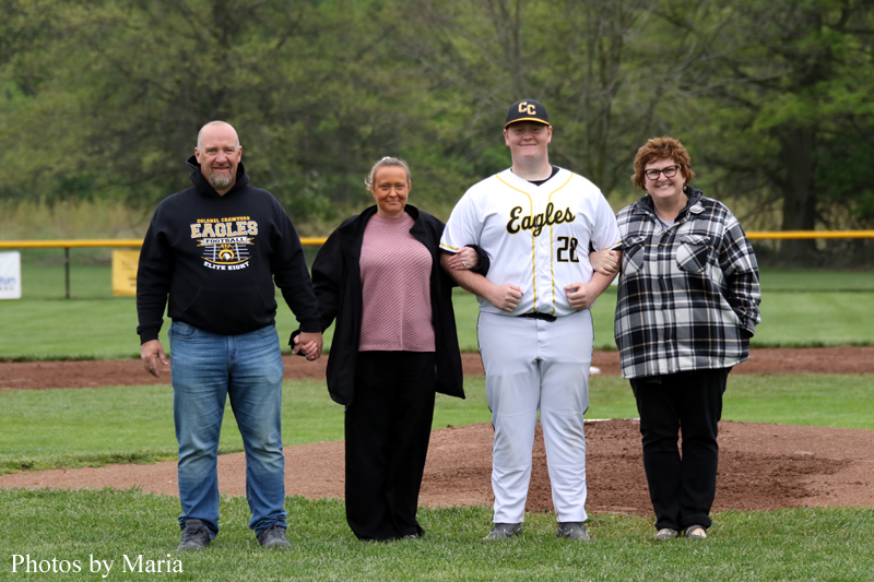 A group of four people standing on a baseball field, the player in a white Eagles uniform is flanked by a man, a woman, and another woman; all hold arms.
