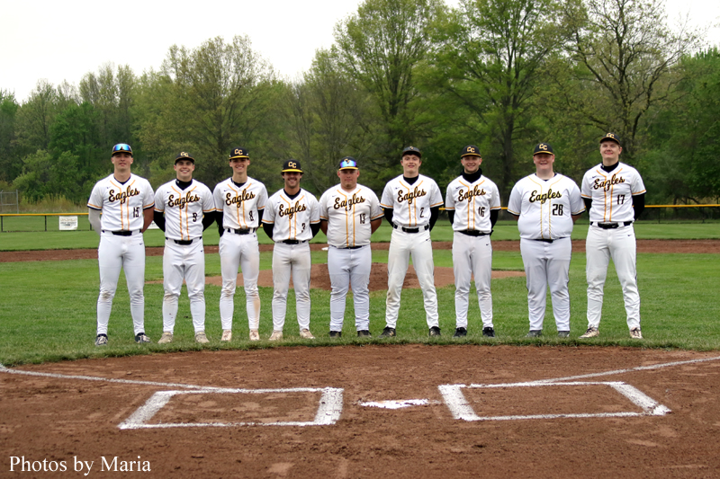 Nine baseball players in white and black 'Eagles' uniforms stand shoulder to shoulder on the infield for a team photo, bases and dirt visible in the foreground.