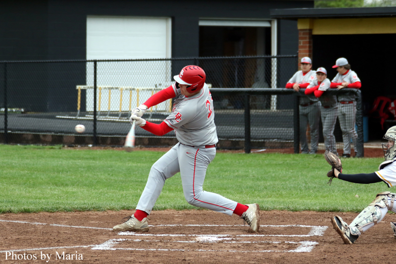 Baseball batter in gray and red swings at a pitch near home plate as the catcher watches in the foreground.