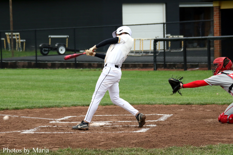Baseball batter in white uniform mid-swing at a pitch, catcher in red crouching behind him on the infield