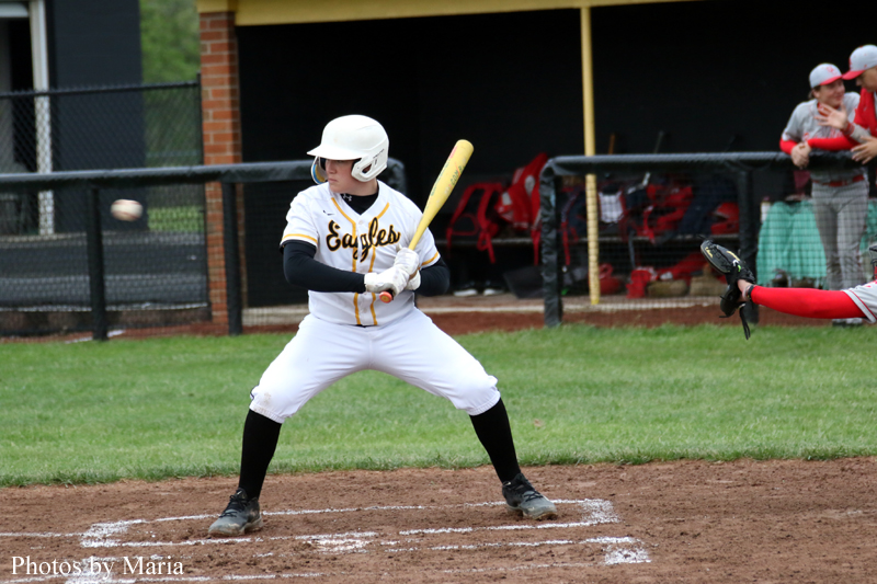 Baseball batter in a white Eagles uniform stands at home plate with a bat raised, ready to swing as the ball approaches.