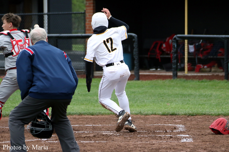 Baseball batter in white uniform number 12 runs toward first base as umpire and catcher stand nearby.
