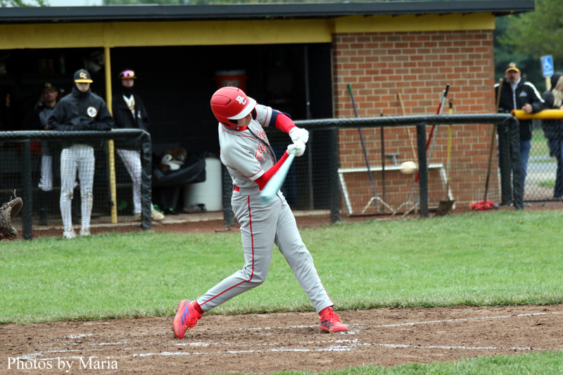 Baseball batter in gray and red uniform swings a teal bat on a dirt infield; dugout and spectators in the background.