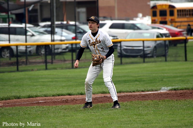 Young baseball infielder in a white Eagles jersey crouches, glove ready on the dirt infield during a game