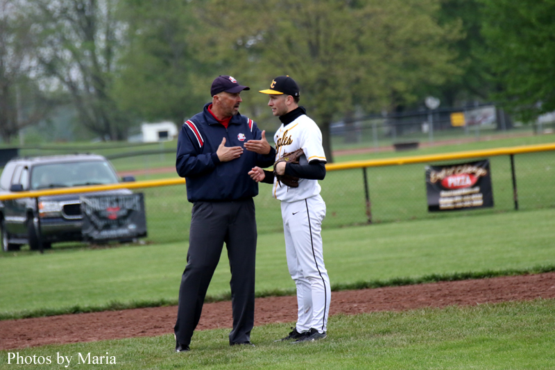 Baseball coach and player in discussion on the infield dirt near the outfield fence.