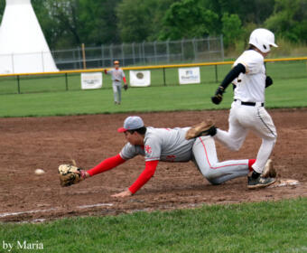Baseball fielder in gray and red dives on the dirt to reach a ground ball as a baserunner in white slides into the base.