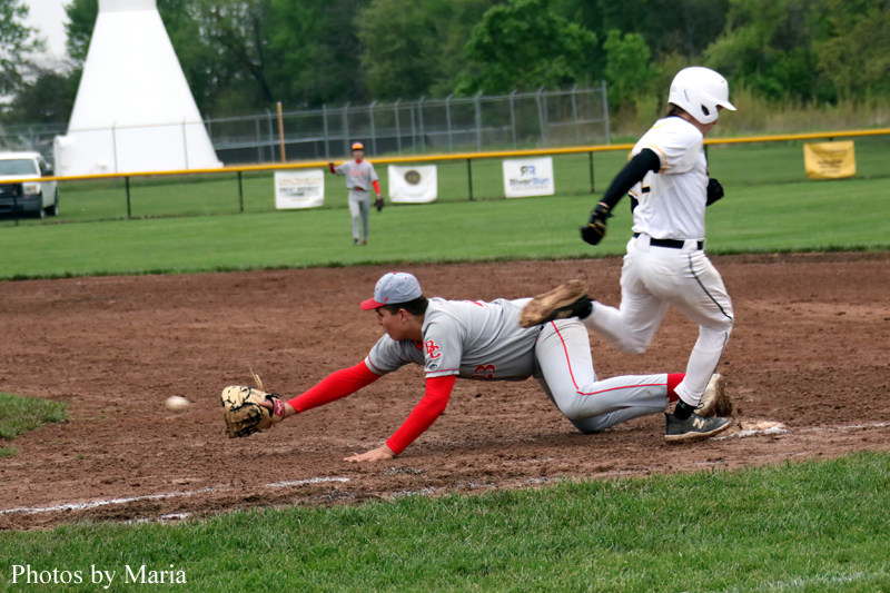 Baseball fielder in gray and red dives on the dirt to reach a ground ball as a baserunner in white slides into the base.