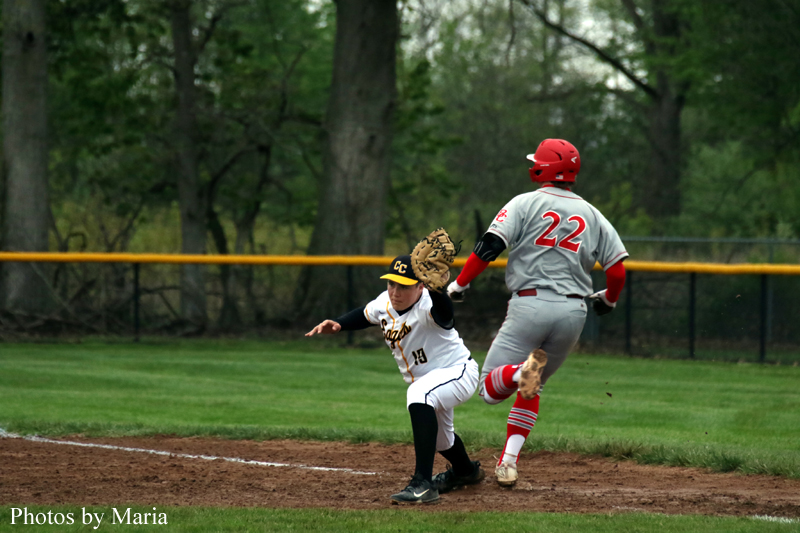 Baseball scene: a runner in white slides into a base as a fielder in gray (number 22) stands nearby on the dirt infield; watermark 'Photos by Maria' visible.